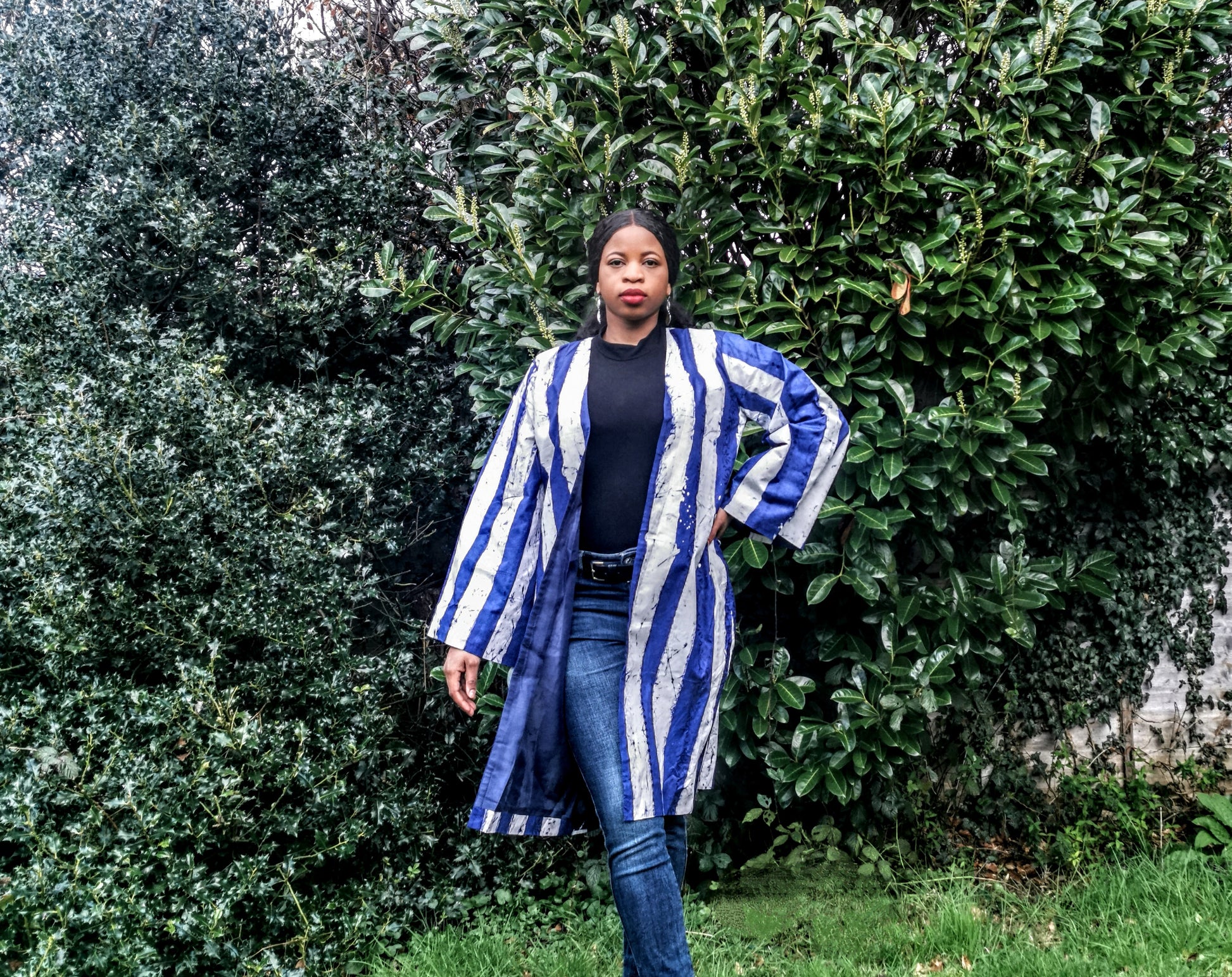 Woman wearing a blue and white striped kimono standing in front of green bushes.