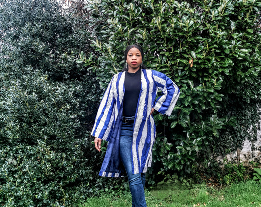 Woman wearing a blue and white striped kimono standing in front of green bushes.